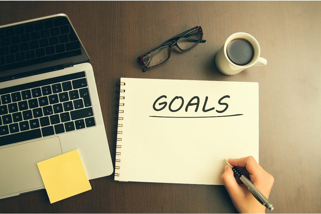 open notebook with handwritten goals beside modern tablet on wooden table recognizing personal value and beliefs that keep moms playing small