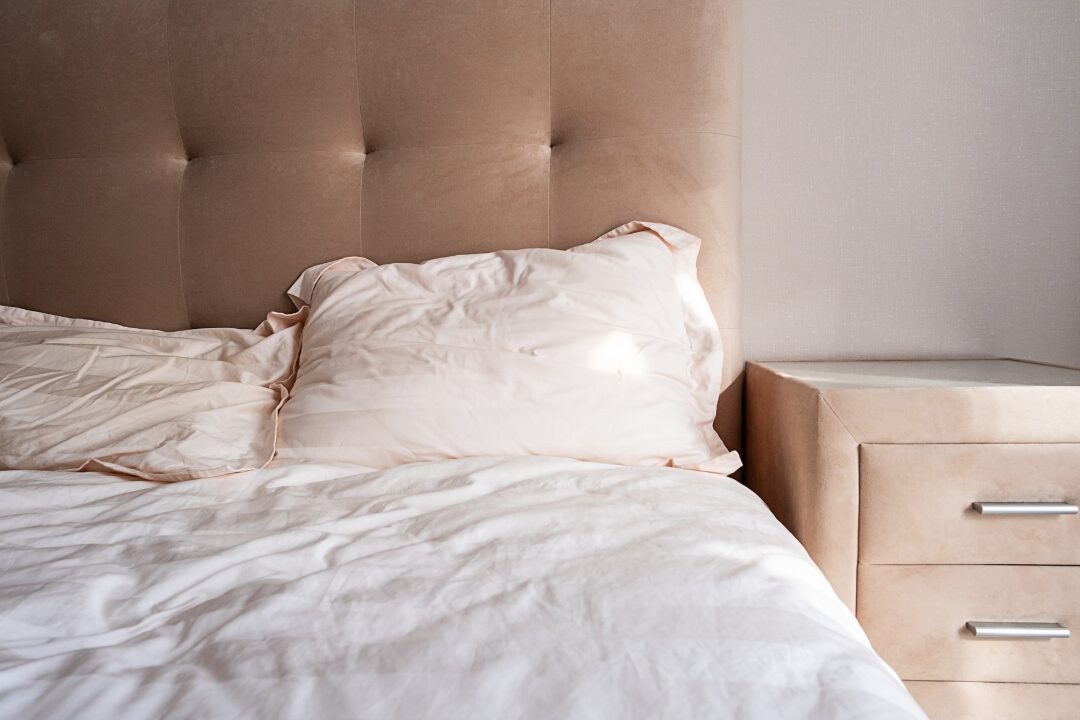 bedroom featuring large soft beige upholstered headboard with linen sheets