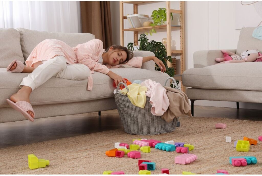 mother laying down and closing eyes amidst scattered toys in living room