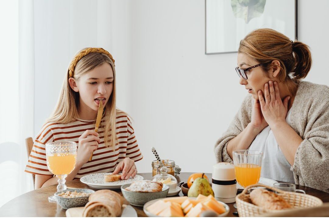 parent and young child sitting across from each other in cozy cafe drinking juice and eating pastry