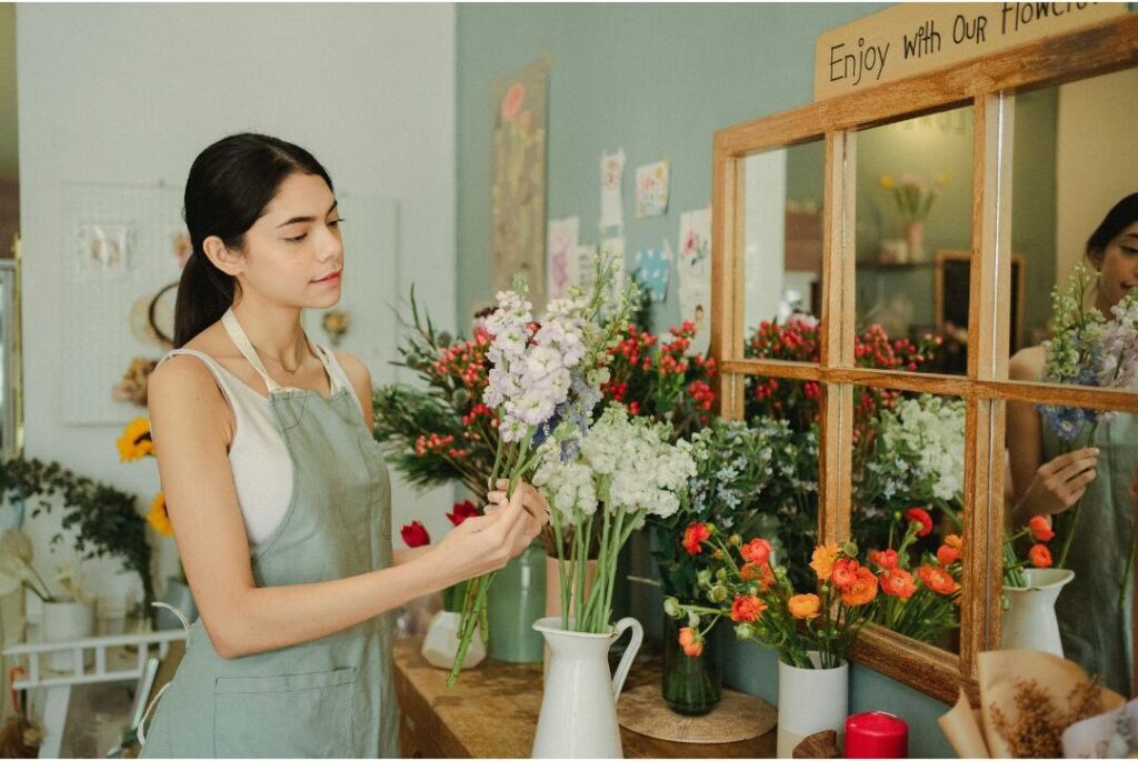 woman placing fresh flowers into glass vase on wooden counter