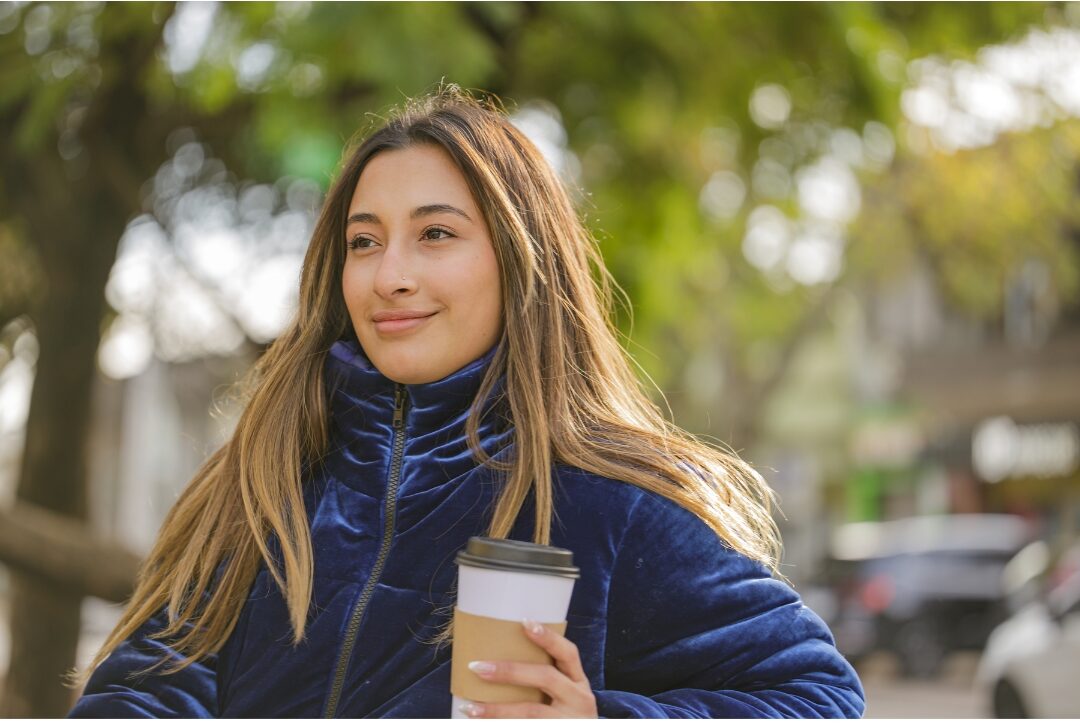 woman sitting on park bench holding warm coffee cup practicing gentle self compassion