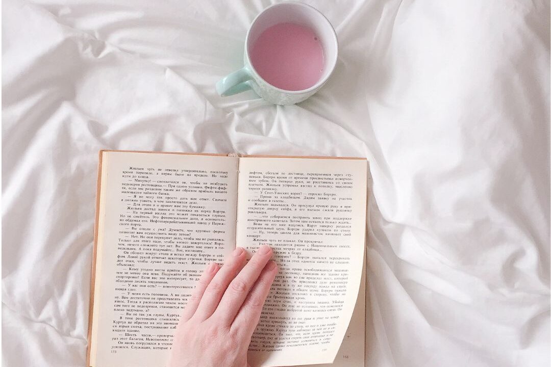 hands holding open hardcover book over cozy linen blanket
