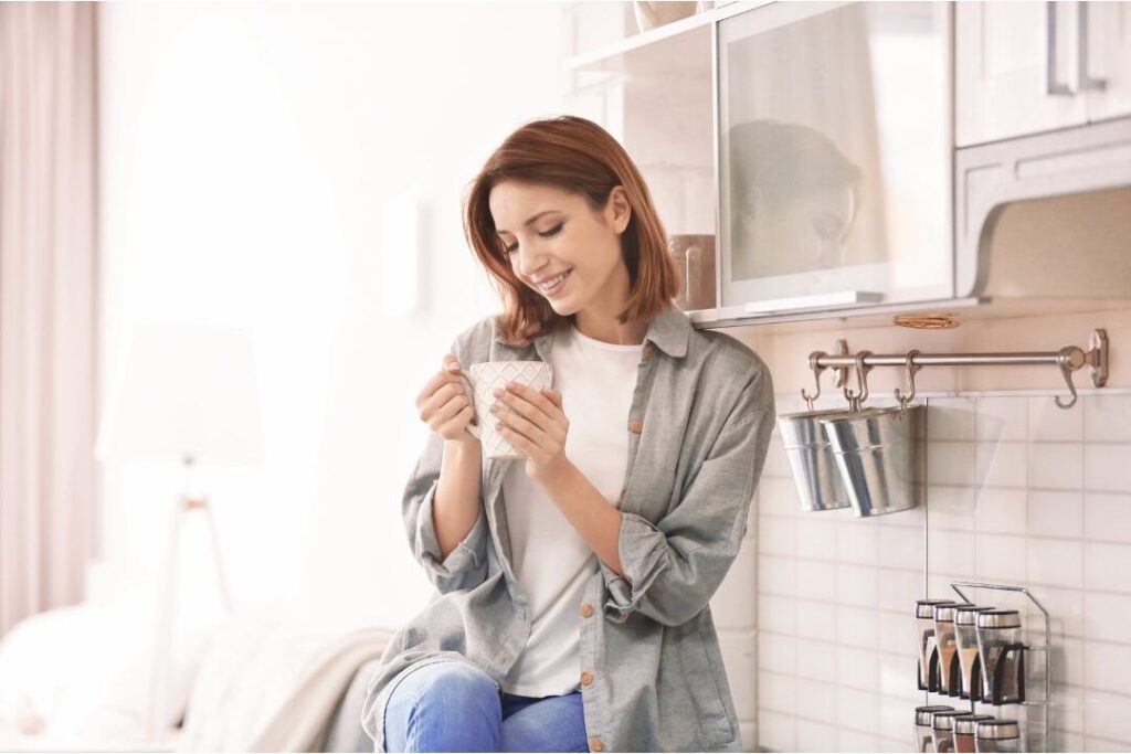 happy woman drinking tea peacefully in serene sunlit kitchen