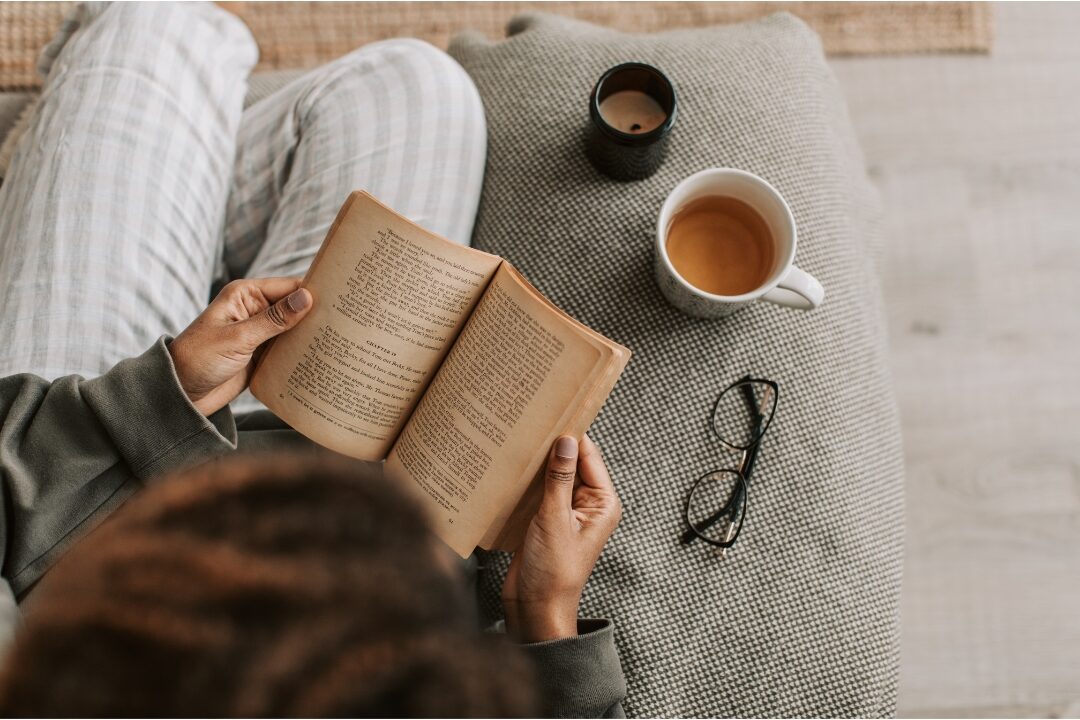 woman sitting comfortably in cozy chair reading a book with warm tea prioritizing personal leisure