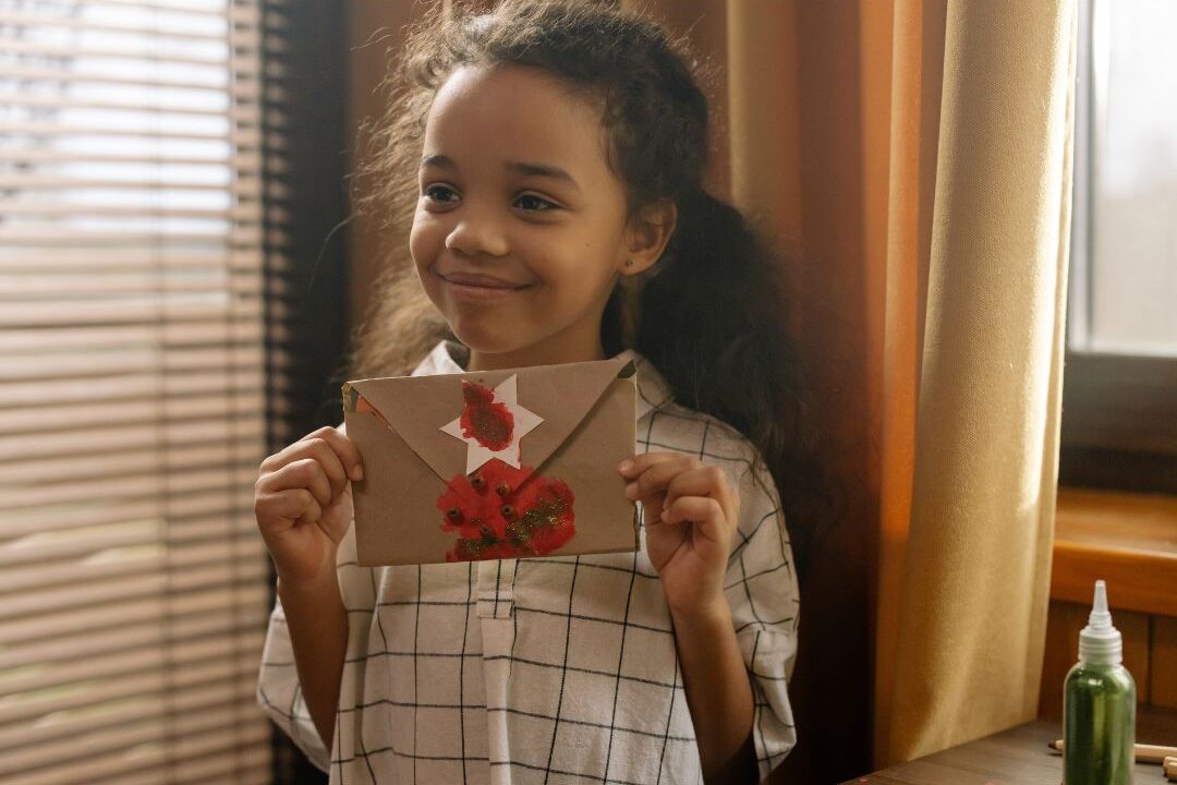 child slipping handwritten encouraging card into colorful envelope on table