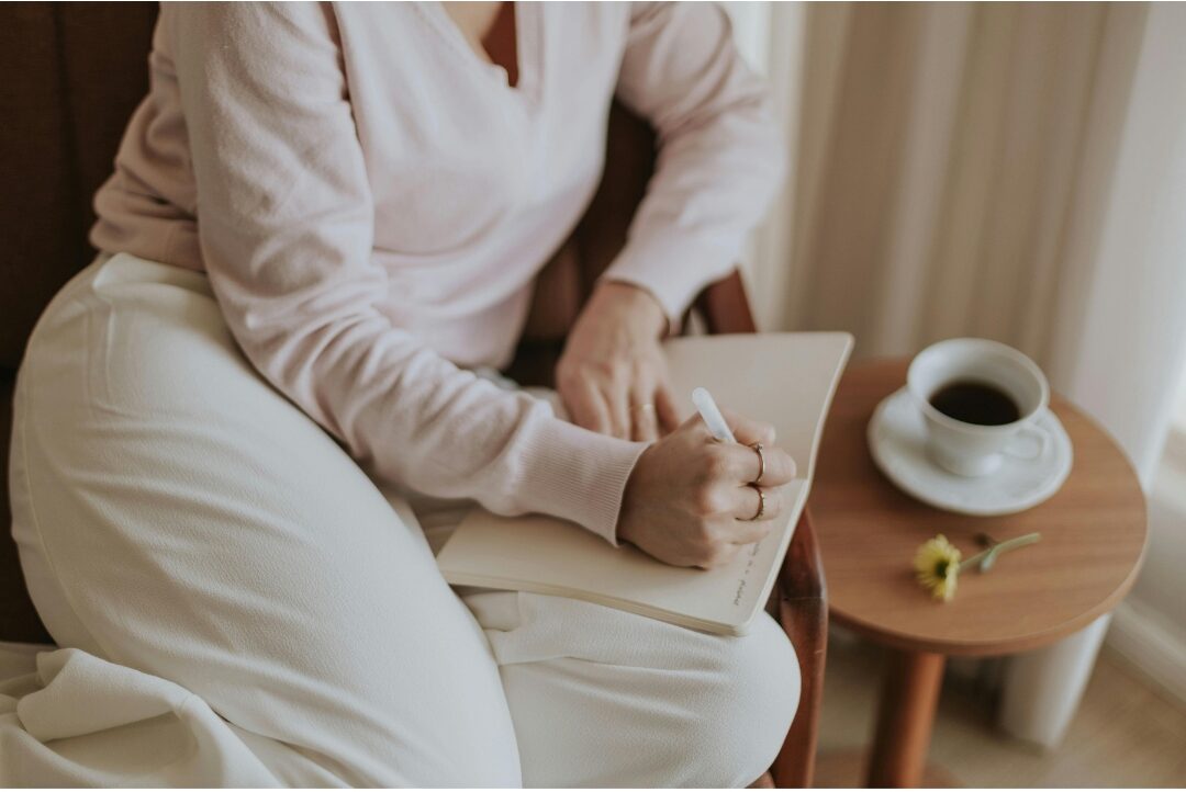 woman writing peacefully in journal while sitting on comfortable armchair understanding why comparison is stealing your joy