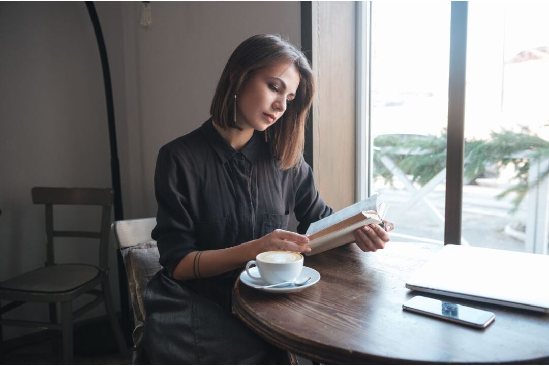woman sitting alone happily reading book at sunlit cafe table