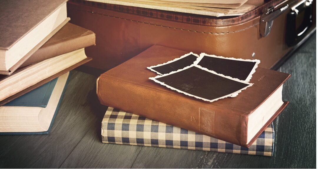 stack of cloth-bound vintage hardcover books on wooden nightstand