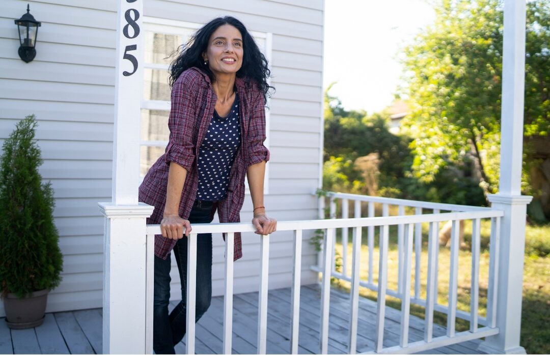 woman standing on sunlit wooden porch looking forward with joyful smile knowing why comparison is stealing your joy