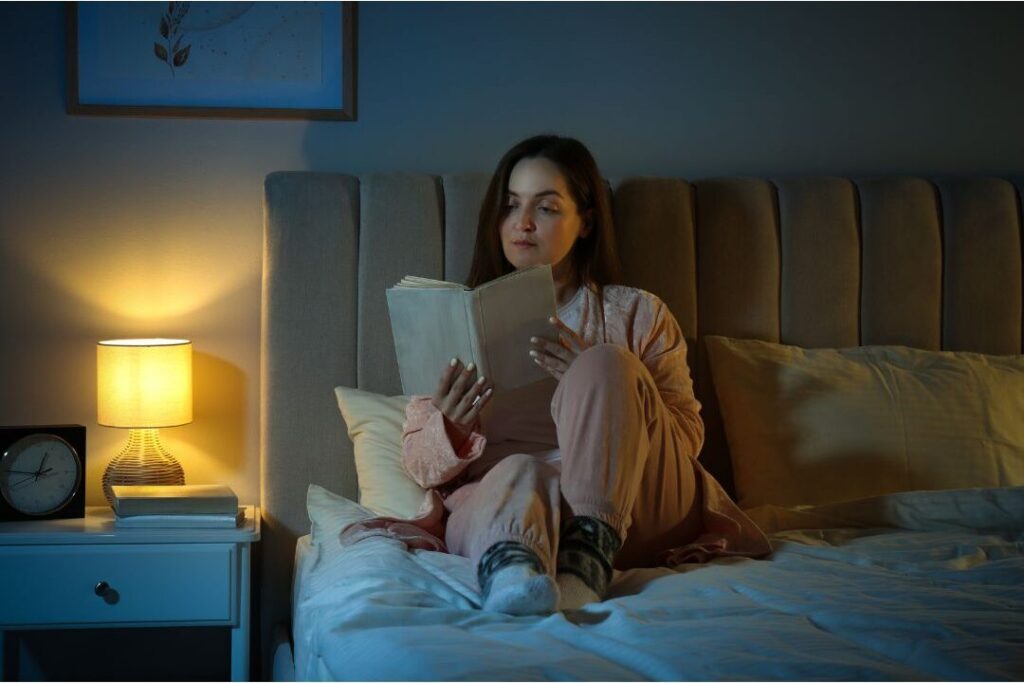 woman reading book in bed with warm bedside lamp lighting
