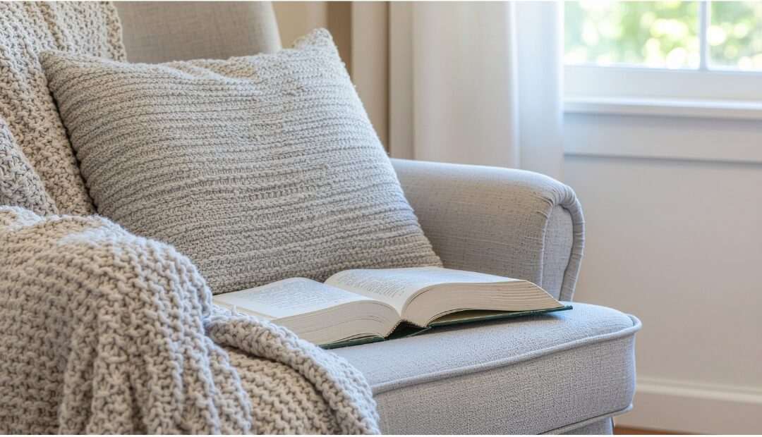 cozy armchair beside window with throw blanket and small book stack