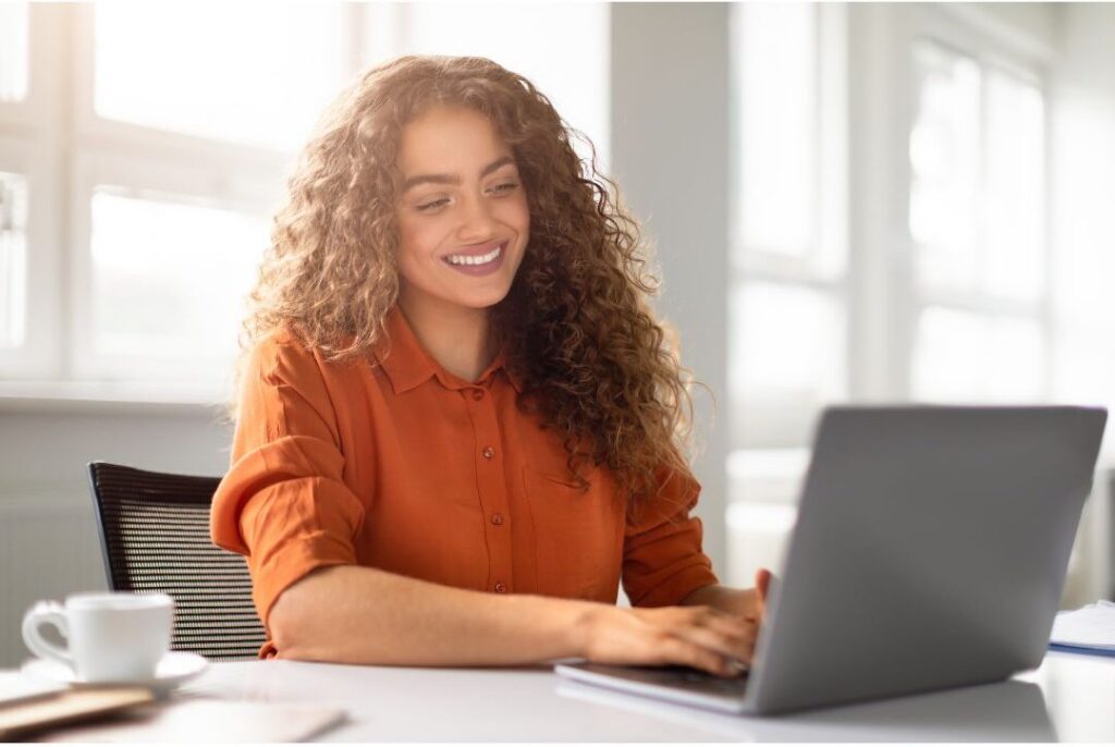 smiling woman working on modern laptop in sunlit room