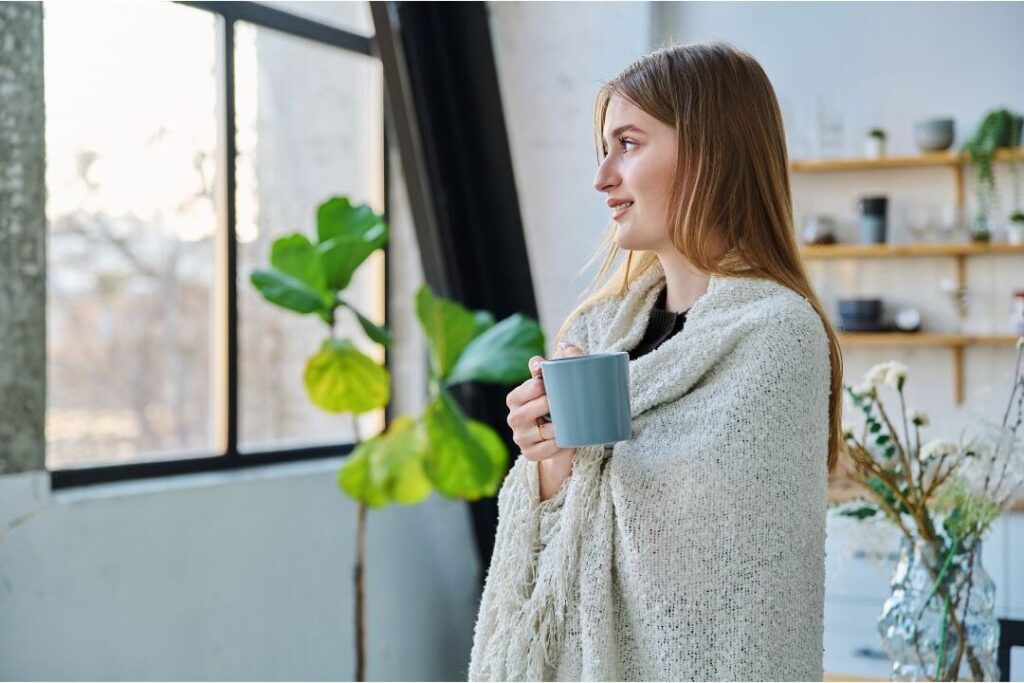 smiling woman holding hot mug looking out sunlit window peacefully illustrating how this one weekly habit eliminated so much stress