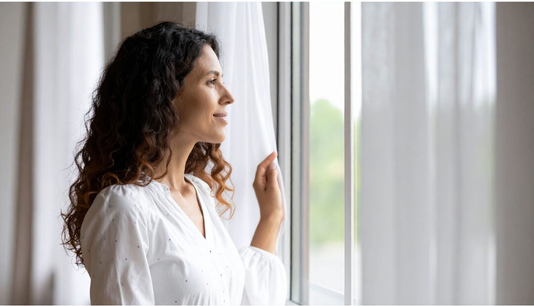 confident serene woman standing by window in bright living room discovering things mentally strong moms do differently