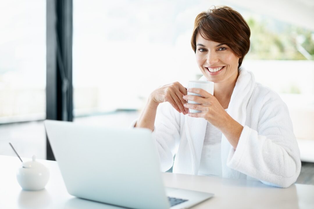 smiling remote working mother drinking coffee at clean desk early morning exploring things successful remote moms do before 9 a.m.