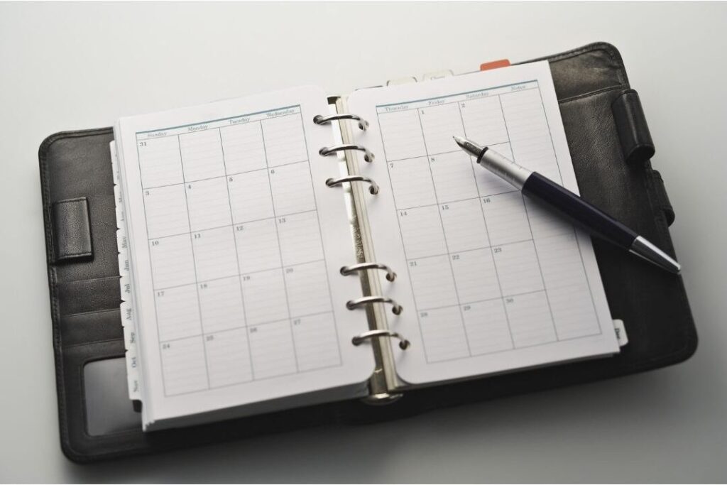 weekly calendar planner open on wooden table with colorful pens
