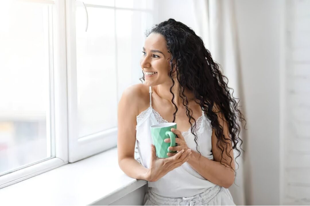 woman holding warm ceramic coffee mug near window with soft sunlight displaying 30 tiny luxuries every woman deserves
