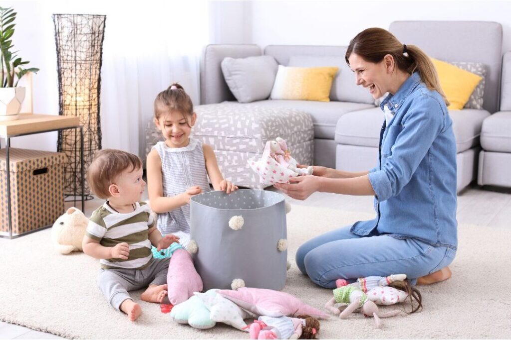 woman carrying wicker basket picking up toys off living room floor