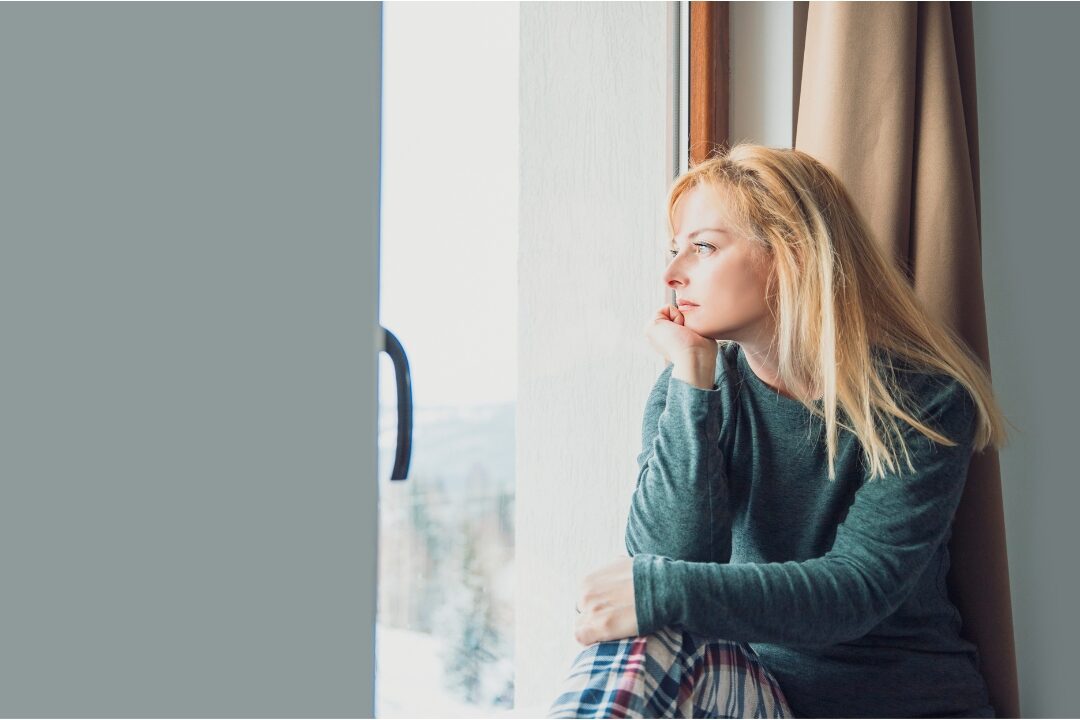 woman sitting quietly on sofa looking out window thoughtfully processing mental exhaustion