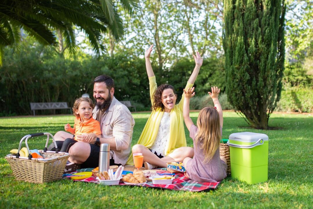 family resting on picnic blanket under large leafy tree