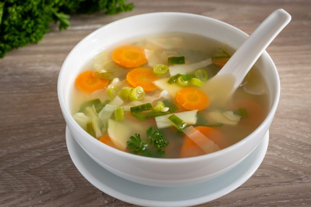 bowl of warm vegetable soup with fresh bread on wooden table