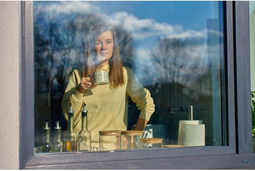peaceful woman drinking hot coffee near bright window explaining why successful moms don't start their day with laundry