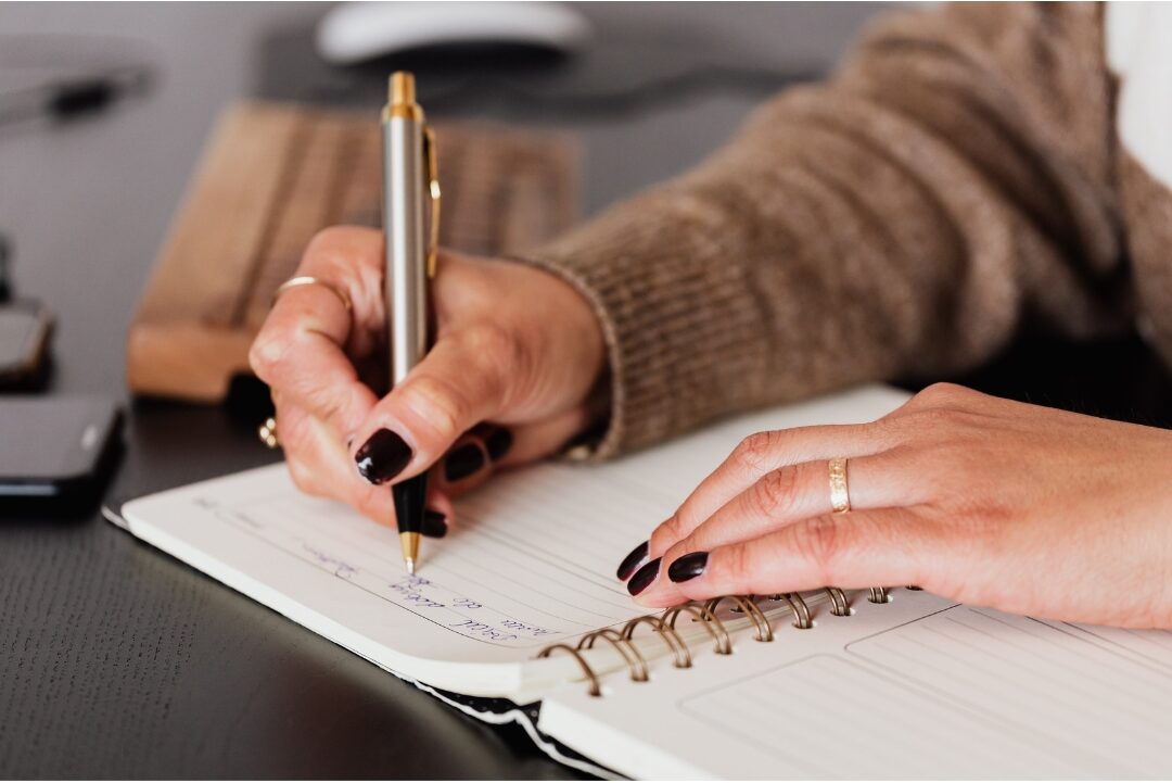 woman checking off item in planner with green pen at clean desk realizing how to stop feeling like you're failing