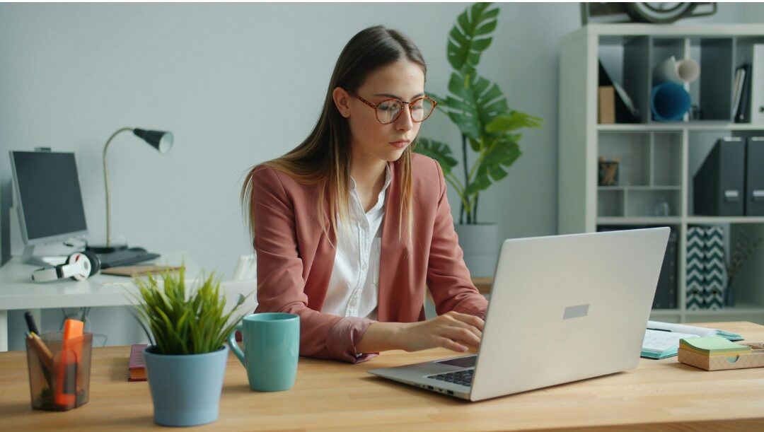 woman working on laptop at tidy wooden desk with determined look overcoming self limiting career beliefs
