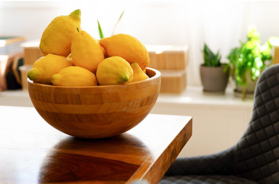 wide wooden bowl filled with fresh lemons sitting on a kitchen counter