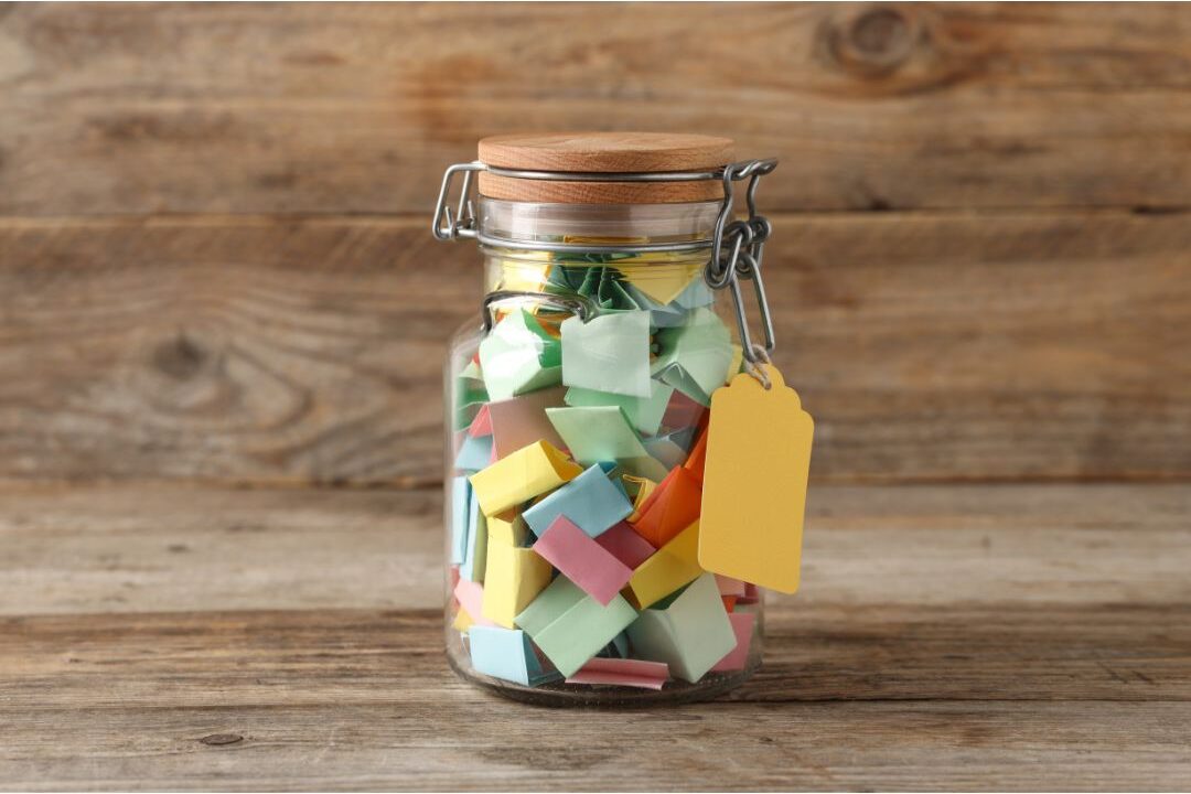 clear glass jar filled with colorful handwritten notes sitting on wooden table