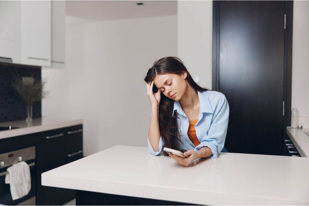 exhausted thoughtful woman sitting at kitchen counter with head in hands realizing you're not lazy you're probably overloaded